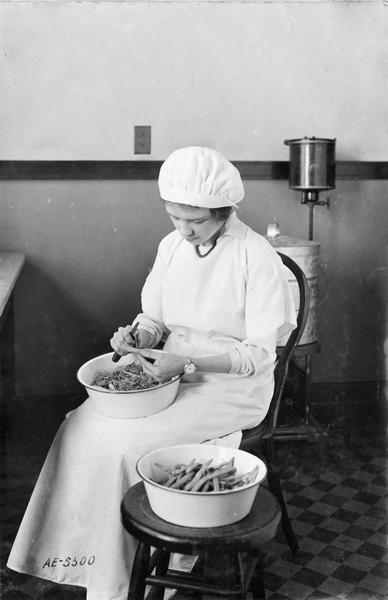 Woman sitting and preparing string beans for canning.