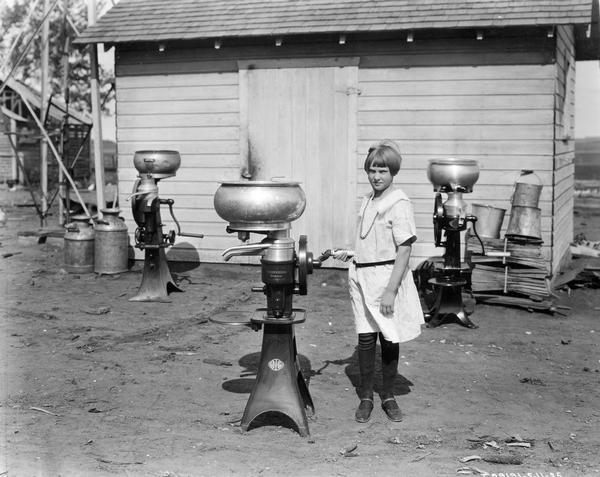 Lucille Schmidt standing in front of a farm building with three McCormick-Deering cream separators.