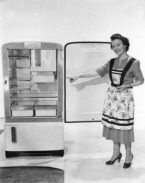 Publicity photograph of Irma Harding pointing out features of a new model refrigerator. Ms. Harding was a fictional character who acted as a  spokesperson for International Harvester refrigerators. The woman here is a model playing the role of "Irma Harding."
