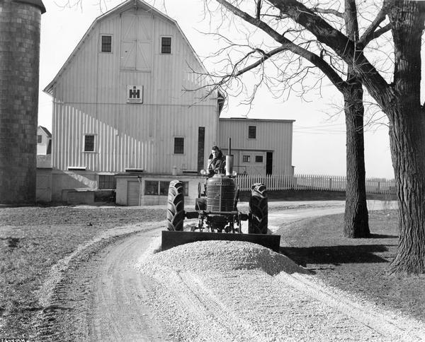 Worker leveling gravel with a McCormick-Deering Farmall M tractor and a no. 7 angle dozer at International Harvester's Hinsdale farm and testing facility.