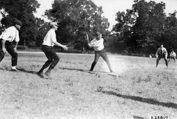 Young men playing baseball in a park or open field. The men may be employees of the International Harvester Company at a factory or office picnic.