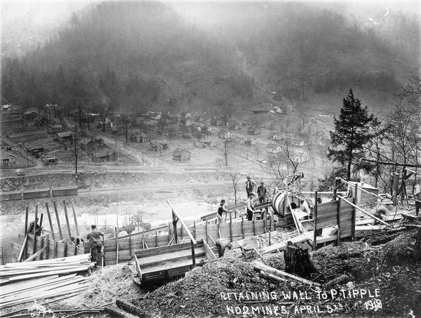 Men working on a hillside retaining wall to "P tipple" of no. 2 mine. Railroad tracks and houses are below in the distance. Benham was a "company town" created by International Harvester for the workers of the Wisconsin Steel Company. Wisconsin Steel was a subsidiary of International Harvester and operated coal mines at Benham.