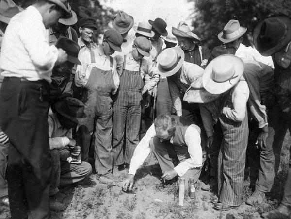 Man, possibly from International Harvester's Agricultural Extension Department, performing an acid test on soil in front of a group of men and boys.
