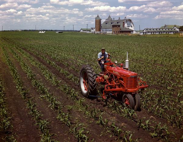 Slightly elevated view of a farmer on a McCormick Farmall H tractor with cultivator at Hinsdale Farm, near International Harvester's experimental farm.