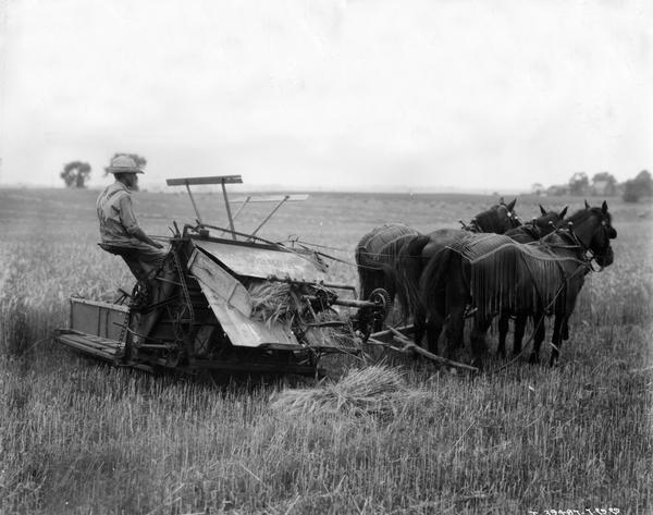 Farmer W.A. Lindvall demonstrating a McCormick grain binder with three horses on his farm. The original caption reads in part: "Took moving pictures and still photographs of binder on Mr. W.A. Lindvall's farm, Belvidere, Illinois, Route 3. The photographs were taken of the machine working in barley. Mr. Lindvall bought this farm a year ago from Mr. Johnson, and this binder was on the farm at the time . . . Our repair books show that this binder was made by [the McCormick Harvesting Machine Company] in 1888 . . ."