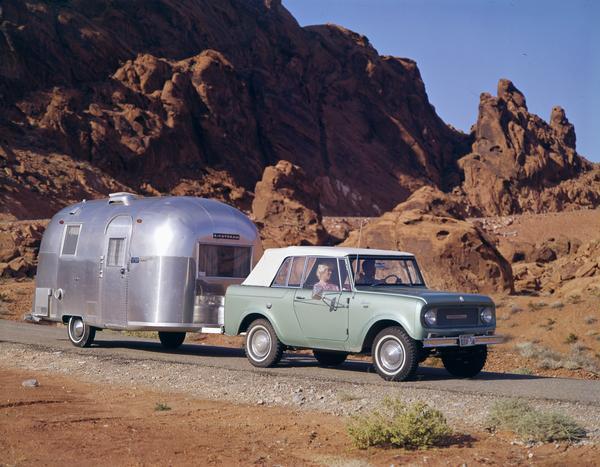 Color advertising photograph of a couple sightseeing in a 1965 International Scout pickup pulling an Airstream camper in the Nevada hills.