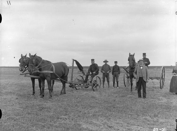Group of farmers posing in a field with a McCormick horse-drawn mower and hay rake. The scene appears to be in France.