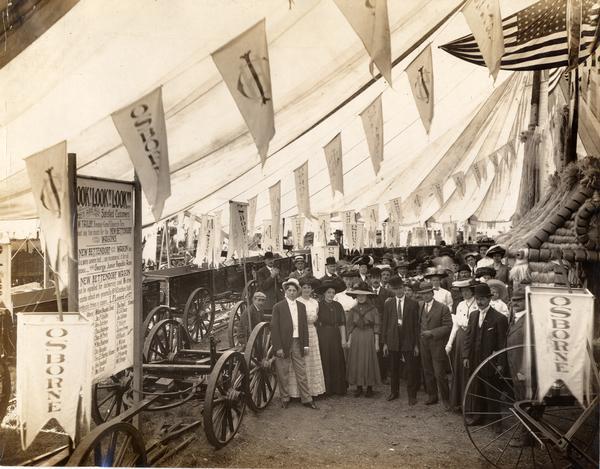 Crowd gathered under a tent to view the new line of Osborne wagons at International Harvester's Osborne Division exhibit at the New York State Fair, September 12-17, 1910.