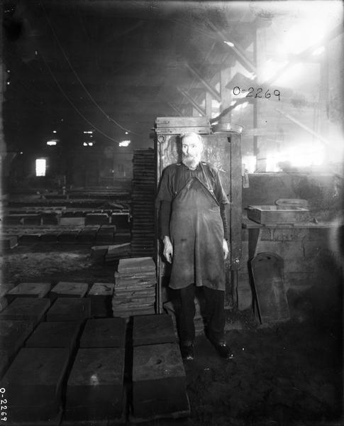 Older factory worker standing among stacks of molds for casting parts. The man most likely worked at International Harvester's Osborne Works.