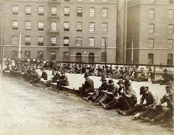 Factory workers eating lunch outside International Harvester's McCormick Works. The factory was owned by the McCormick Harvesting Machine Company before 1902.