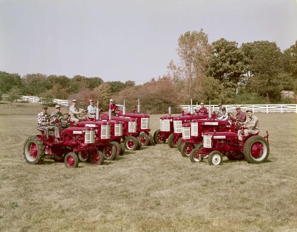 Group portrait of men seated on Farmall and International tractors for 1957 assembled in two rows in a V-shaped formation. Pictured here (L to R) are: Farmall Cub, Farmall 130, Farmall 230, Farmall 350, Farmall 450, International 650 Diesel, International W450 "Wheatland," International 350, International 130, and International Cub Lo-Boy.
