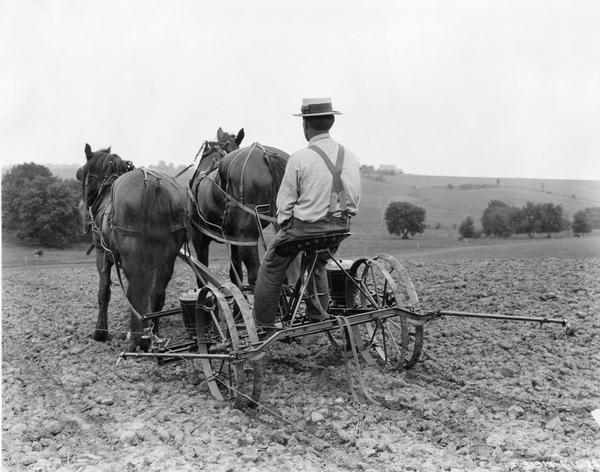 Rear view of farmer LeRoy Hansen in a field with a horse-drawn McCormick-Deering corn planter.