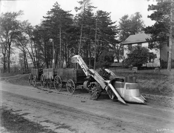 Farmer Elmer Petersen driving a Farmall tractor with attached corn picker and three wagons along rural Route 2. Original caption reads: "The picture shows Mr. Petersen starting for the farm owned by A.H. Essington, Route 3, Clifton, Illinois."