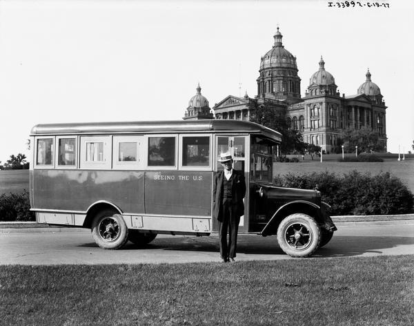 Man posing with an International tour bus in front of the Iowa State Capitol building. The sign painted on the side of the bus reads: "Seeing the US."
