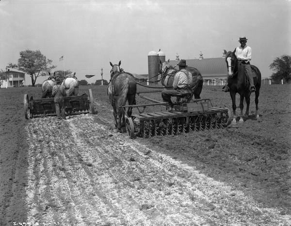 Farmers in a field with a horse-drawn McCormick-Deering lime sower and rotary hoe. To the right is a man sitting on a horse.