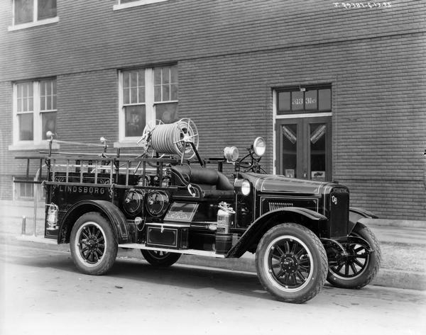 International Model S 1925 fire truck, owned by the city of Lindsborg, parked on a street in front of a brick building.