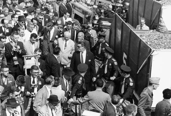 Elevated view of Soviet Premier Nikita Khrushchev wading through a throng of reporters during a visit to a farm. A Farmall 560 tractor is in the background. Roswell "Bob" Garst (right), and Ambassador Henry Cabot Lodge (left), are leading Khrushchev through the crowd.