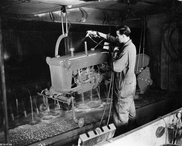 Factory worker painting a Farmall Cub tractor in a paint booth at International Harvester's Louisville Works. Original caption notes that the worker is not wearing a mask.