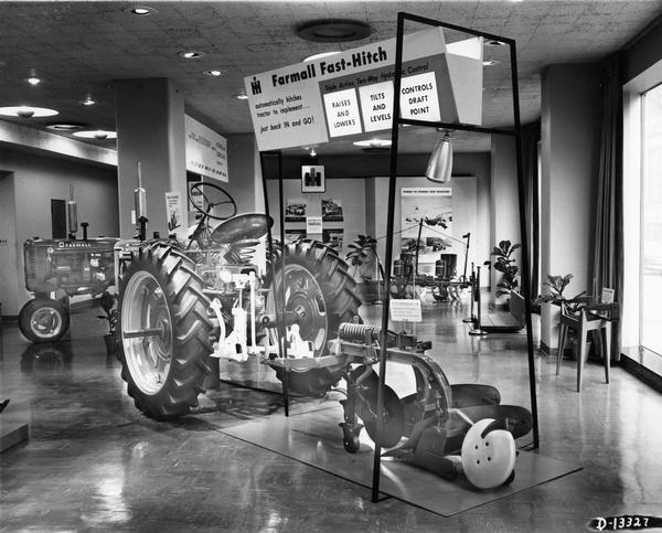 Exhibit in the showroom at International Harvester's General Office demonstrating the features of the Farmall Fast-Hitch. The exhibit features a Farmall Super C tractor with an attached Fast-Hitch plow in what appears to be an automated moving display. The fast hitch mechanism has been painted white for display purposes.