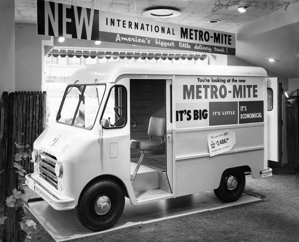 International Metro-Mite Showroom display featuring the International Metro-Mite AM-80 truck.  A banner above the Metro-Mite describes the vehicle as "America's biggest little delivery truck!" The sign on the truck reads: "You're looking at the new Metro-Mite it's big it's little it's economical".