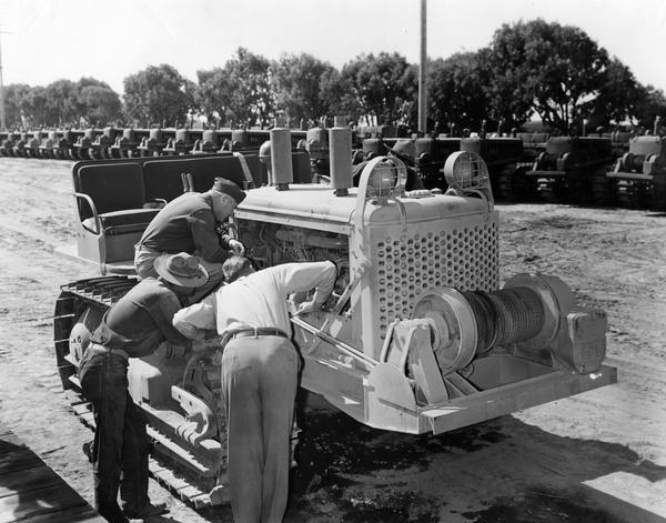 U.S. Military Crawler Tractors Men examining an International crawler tractor (TracTracTor). The original caption reads: "J.M. Curtis, Los Angeles branch industrial traveler (no hat), explaining some of the details of servicing the starting mechanism to Major Moffitt and PFC Evans at the Camp Callan ordnance tractor depot."