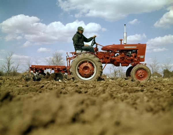 Right side profile view of a man pulling a 122 disk harrow through a field with a Farmall 140 tractor.