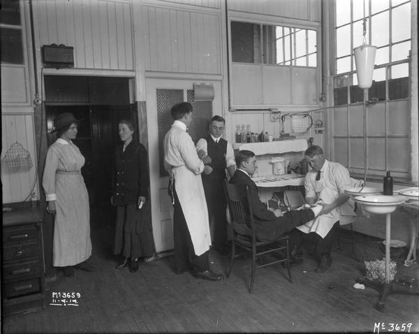 Medical staff attending to male and female factory workers at International Harvester's McCormick Works. The factory was owned by the McCormick Harvesting Machine Company until 1902 when it became International Harvester's McCormick Works. It was located at Blue Island and Western Avenues in the Chicago subdivision called "Canalport."