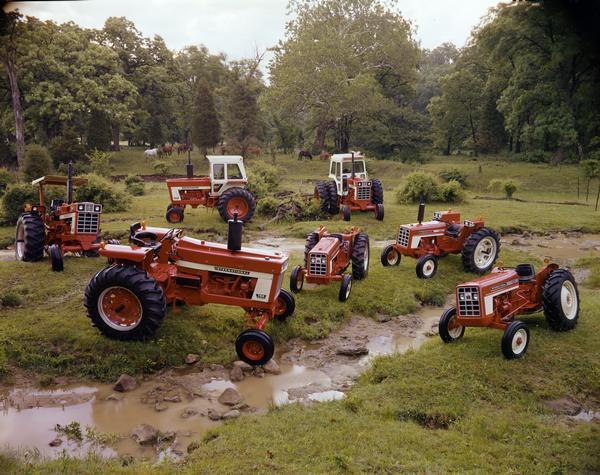 Color advertising photograph of the International tractor family arranged for display around a rural creek. Tractors include (from front, clockwise): Farmall 766, Farmall 1466 Turbo, Farmall 966, Farmall 1066 Turbo(?), 574, 354, and 454.