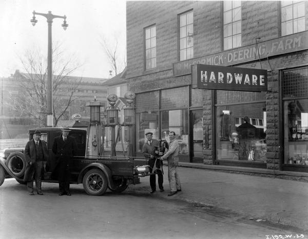Men loading a cream separator and gas pumps into the back of an International Red Baby truck in front of the Landall Brothers hardware store and farm equipment dealership. Signs on the building read: "Hardware" and "McCormick-Deering Farm [Equipment]".