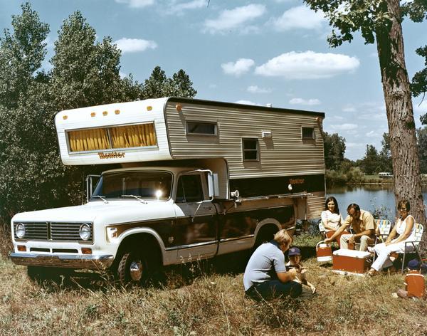 Color advertising photograph of a family camping near a lake with an International 1310 pickup truck and a Monitor camper.
