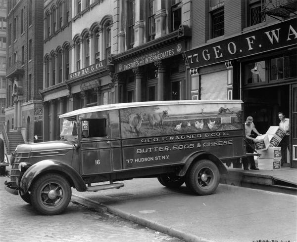 Men loading cases of eggs onto an International D-30 truck parked in front of Geo. F. Wagner & Co. Inc. The truck has a farm scene painted on the side, including cows and chickens.