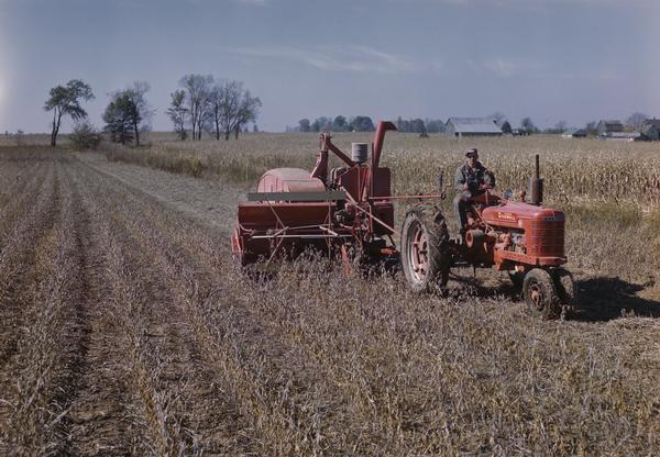 Farmer harvesting grain with a Farmall H tractor and harvester-thresher (combine).