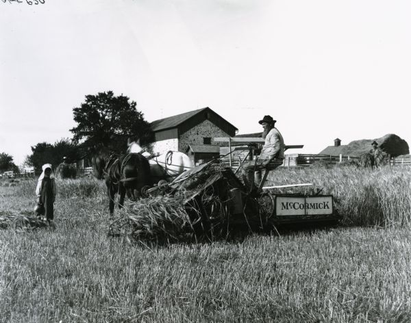 European(?) farmer harvesting grain with a horse-drawn McCormick grain binder as a young girl with water jug looks on. Two farm hands are in the background bundling grain.