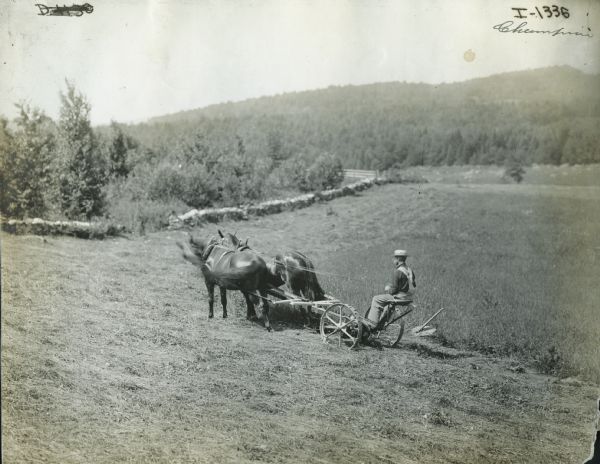 A man drives two horses uphill, pulling a Champion sickle-bar mower.