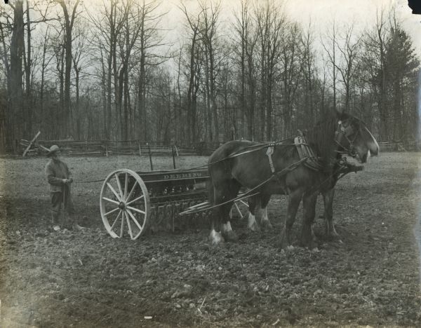 A farmer is walking behind a horse-drawn Deering grain drill.