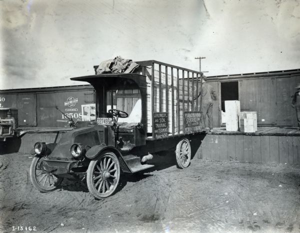 International F-31 truck backed up to a train car for loading. The truck was operated by J.P. Kennedy and Son Trucking and Teaming. A sign at the back of the truck advertises piano moving, storage and any heavy trucking.
