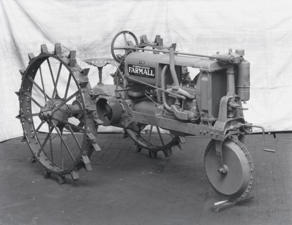 Engineering photograph of a Farmall F-12 tractor with a single front wheel. There is a backdrop on the wall in the background.