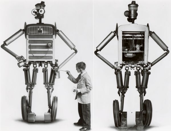 Front and rear view of "Tracto," a robot made of tractor parts for International Harvester's exhibits at state fairs. The front view features a young boy in tie and sports coat who appears to be touching Tracto's hand with a screwdriver, and holding a square object with the International Harvester logo in the other. Tracto poses with oil can and a can of IH tractor Hy-Tran fluid. From the original press release: "the eight-foot 'talking' robot is assembled from 227 farm tractor and implement parts. Robot is equipped with two-way communication system and contains motor gear reducer for oscillating head and lifting right arm. Electrically powered, eyes light up through transformer installed in robot's stomach." According to another press release, Tracto was voiced by "district office personnel hidden from the view of passers-by, but advantageously located to spot interested viewers and provoke them into conversations."