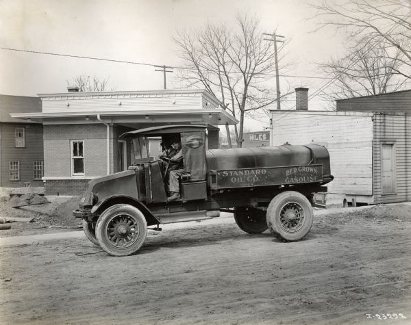 Two men sit in an International Model G-61 truck on a dirt road. The truck was operated by L.P. Torensen's Standard Oil Company, located at 1305 Maple Street.