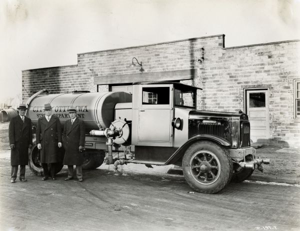 Three men standing in front of an International street cleaning truck. The sign on the side of the truck says: "City of Ottumwa Street Department".