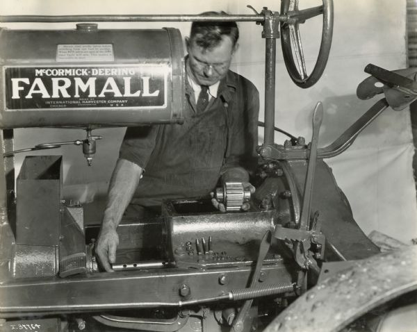 A man wearing overalls and a work suit overhauls a Farmall Regular tractor.