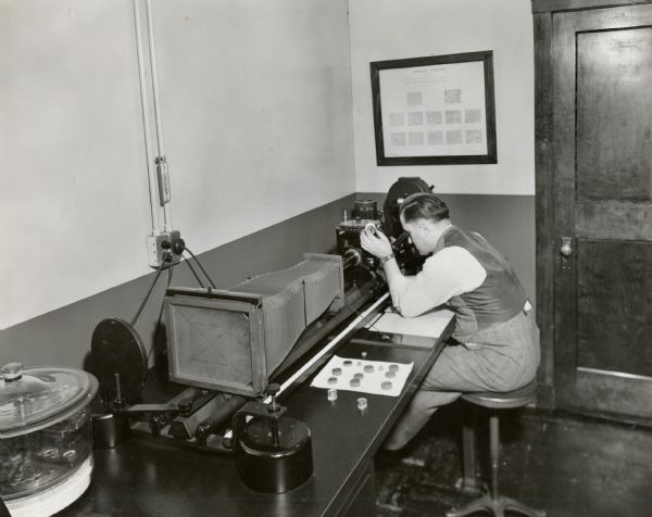 William Koppa uses a microscope to examine a specimen of steel. The original caption reads: "Micro-photography is employed at International Harvester's Gas Power Engineering Department, at Chicago, to study the structure of metals. This camera magnifies up to 4,000 times. William Koppa is examining a specimen of steel at the microscope."