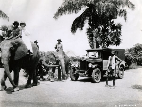 Men on elephants near an International Special Delivery truck at the "Mission in Buta" in the Belgian Congo.  Most of the men ride on elephants while one stands beside the automobile. The truck was part of an International Harvester sponsored expedition to drive across Africa. The man on the lead elephant is likely Clyde N. King, of International Harvester.