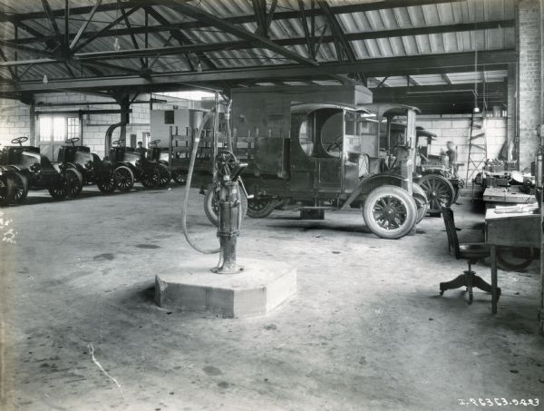 Desks are along a wall of windows in a shop area, while trucks are lined up on the floor behind them, possibly at the International Harvester Company No. 3 sales and service station.