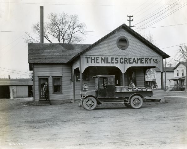 Men stand in front of The Niles Creamery Company alongside a truck loaded with milk pails.