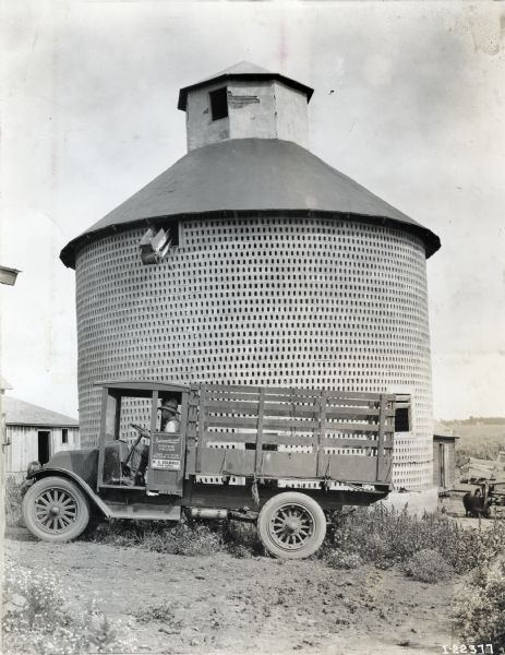 International F-31 Truck Operated by W.H. Brammer International model "F" "31" truck operated by W.H. Brammer of Coon Rapids. There is a man in the driver's seat, and a silo behind the truck.