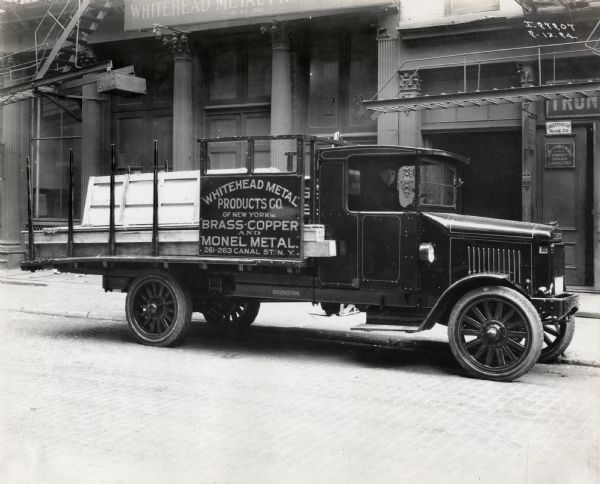 International Model 63 truck operated by Whitehead Metal Products Co. of New York. The truck was photographed outside the Whitehead Metal Products Co. with a man in the driver's seat. Printed on the side of the truck is the company's name, address, and "Brass-Copper and Monel Metal."
