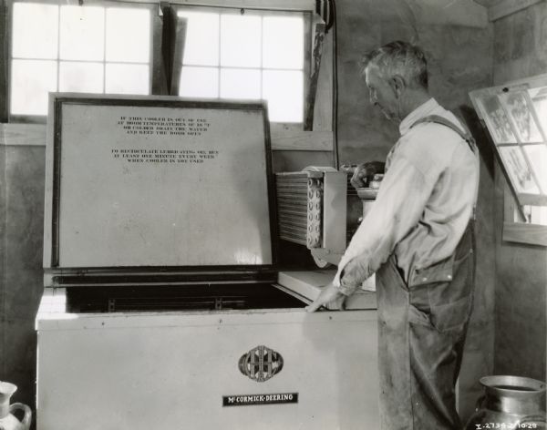 A older man stands next to a McCormick-Deering milk cooler.  Handwritten notes identify the photograph as being taken in Bowling Green, Missouri, and the man pictured as J.H. Tophinke.