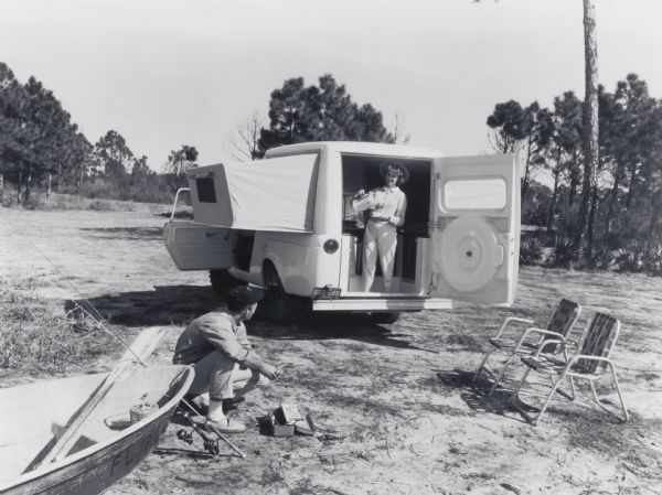 Advertising photograph of a Scout Camper with "bed 'wings' extended." A woman is pouring coffee at the back door, and outside a man by a canoe is readying his fishing gear. Accompanying press release states: "Open the back door of a new Scout de luxe [<i>sic</i>] Camper by International and you step into a modern compact home on wheels. The tended 'wings' of the house are foam-padded beds. Inside is a stand-up galley complete with range, sink, refrigerator, and an adjoining dinette table and benches. A chemical toilet hidden in the wall can be pulled out and screened from view. There are screened windows in the bedroom wings, and screens can be obtained for the Scout front door windows. Also available is a canopy to form a roofed patio at the Scout Camper's back door. Power for the all-wheel drive Scout Camper is provided by a 93 hp. Comanche engine."
