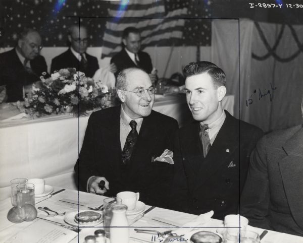 Harold F. McCormick and William E. Hamilton sitting at a table at a 4-H Club award event. The original caption reads: "Harold F. McCormick, Chairman of the Board of Directors, was special host to Wm. E. Hamilton, Good Hope, Illinois, winner of the President's Trophy, national award for achievement covering entire 4-H Club career of the recipient."
